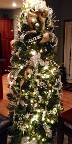 a christmas tree decorated with gold and silver ornaments, bows and lights in a living room