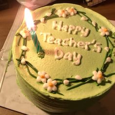 a green cake with white flowers and a single lit candle on it that says happy teacher's day