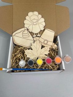 an open cardboard box filled with paint and wooden cutout art supplies, including flowers