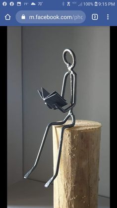 a metal figure sitting on top of a wooden stump holding a book in it's hands