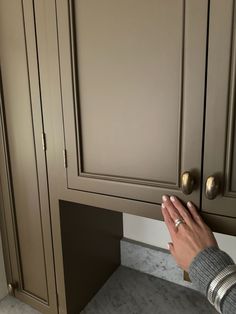 a person is holding their hand up to the door handle on a kitchen cabinet with marble countertops