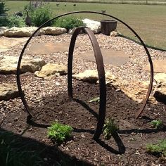 a metal sculpture sitting in the middle of a garden with rocks and plants around it