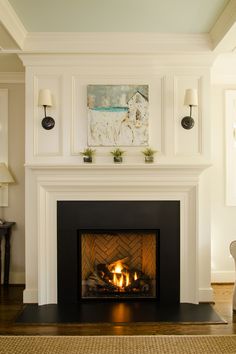 a fire place in a living room with a painting on the wall and two lamps above it