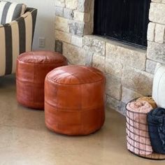 two leather stools sitting in front of a fireplace with pillows and blankets on the floor