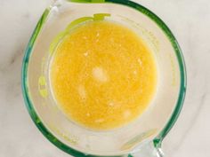 a blender filled with yellow liquid on top of a white countertop next to a green measuring cup