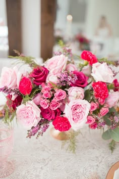 a vase filled with lots of pink and red flowers on top of a white table