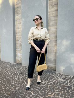 Look com calça cenoura preta, camisa bege, bolsa bege, sapatilha bicolor bege com preta.