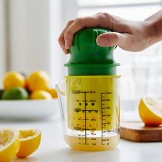 a hand holding a green and yellow blender with lemons in the back ground