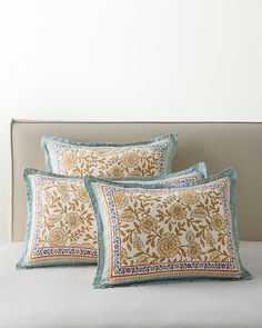 two pillows on a bed with white sheets and blue trimmings, one has an orange flower design