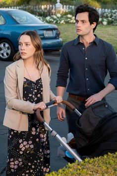 a man and woman standing next to each other in a parking lot with cars behind them