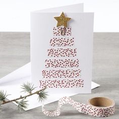 a card with a christmas tree on it next to a roll of tape and a sprig of pine