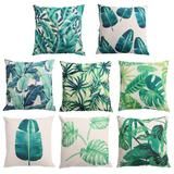 six different green and white pillows with leaves on the front, one has a blue flower