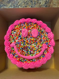 a pink cake with sprinkles and smiley face on top in a box