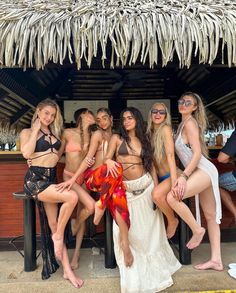 four women in bikinis posing for a photo at a beach bar with straw umbrella