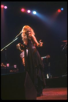 a woman standing on top of a stage with a microphone in her hand and lights behind her