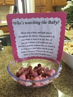 a bowl filled with hearts sitting on top of a counter next to a sign that says who's watching the baby?