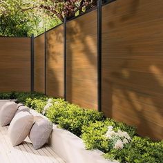 an outdoor seating area with pillows and flowers on the ground next to a wooden fence