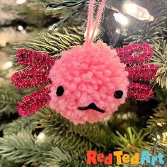 a pink pom pom ornament hanging from a christmas tree