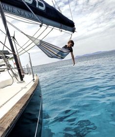 a person hanging from a hammock in the water on a sailboat,