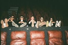 four people sitting in front of a row of brown couches with their feet up