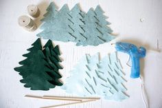 some felt trees are sitting on the table next to yarn and glue bottles with scissors