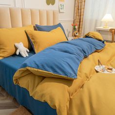 a bed with yellow and blue sheets, pillows and a stuffed animal sitting on it