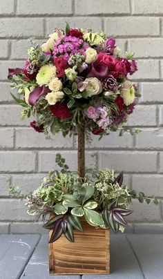 an arrangement of flowers in a wooden vase on a table next to a brick wall