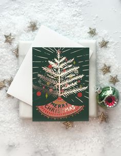 a christmas card sitting on top of snow covered ground next to a green ornament