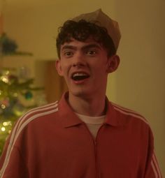 a young man wearing a paper hat in front of a christmas tree with his mouth open