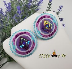 These are authentic Native American earrings, hand crafted by a member of the Muskogee Creek Tribe. Used in the handmade process are seed beads, acrylic cabochons and faux leather backing. The bead colors included in this pair are: alabaster white, teal green and purple seed beads. They measure 1 1/2 inches wide and 1 1/2 inches long. They have stainless steel hypo-allergenic lever back ear post for pierced ears.