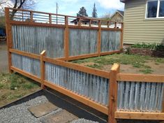 a fence made out of metal and wood in front of a house with gravel on the ground