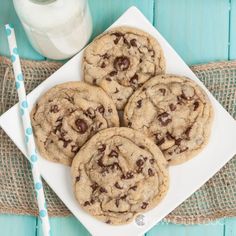 chocolate chip cookies on a white plate next to a glass of milk and straws