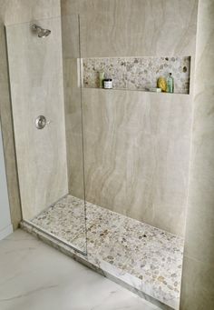 a walk in shower sitting next to a white tiled wall and counter top with shelves on each side