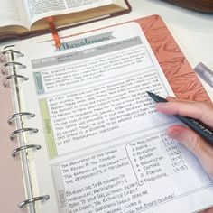 a person is holding a pen and looking at a book with writing on the pages