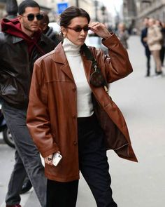 Bella Hadid Brown Leather Coat The fashion icon and diva, Bella Hadid, is the most popular and highly influential supermodel of our generation. Being the source of style inspiration, Bella showcases the off-duty model aesthetic like no other, making her outfits effortlessly chic and trendsetting. Introducing the epitome of urban sophistication with our Bella Hadid brown oversized leather coat, an ultimate wardrobe essential and the perfect addition to your outerwear collection. Striking the perfect balance between casual and formal, this brown leather coat can be effortlessly styled with daily outfits or for important events, showcasing its versatility. Crafted to perfection using premium-quality 100% real leather, this brown jacket is highly durable against winds, scratches, and external Oversized Leather Coat, Collarless Leather Jacket, Red Jacket Leather, Celebrity Inspired Outfits, Brown Leather Coat, Blue Leather Jacket, Leather Jacket With Hood, Fur Clothing, Hadid Style