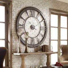 a large clock mounted to the side of a brick wall next to a table and chairs