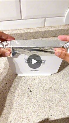 two hands are opening up a box with foil on the bottom and one hand is holding something in it