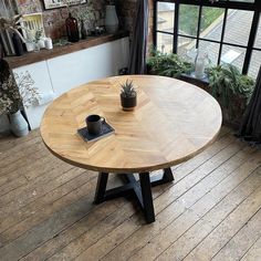 a round wooden table sitting in front of a window next to a potted plant