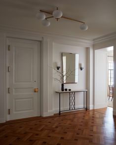 an empty room with wood flooring and white walls, mirrors on the wall and a console table