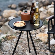 a table with two beer bottles and some food on it next to a chair by the water