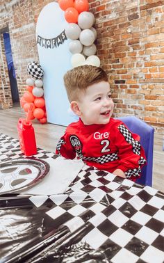 a young boy sitting at a table with balloons in the background