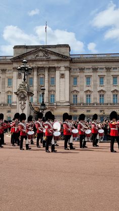 a group of men in red and black uniforms playing drums on the street near a large building