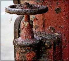 an old rusted fire hydrant sitting next to a red wall