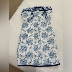 a blue and white floral dress laying on top of a bed next to a pillow