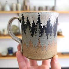 a hand holding a coffee cup with trees on the outside and brown, black, and white glaze