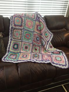 a crocheted granny blanket sitting on top of a brown couch next to a window