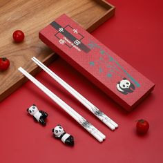 two chopsticks and some tomatoes on a red surface next to a pair of chopsticks