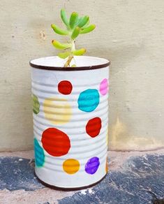 a painted tin can with a small potted plant in the middle and multicolored dots on it