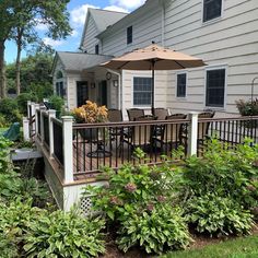 a patio with an umbrella and chairs on the deck next to some plants in front of a house