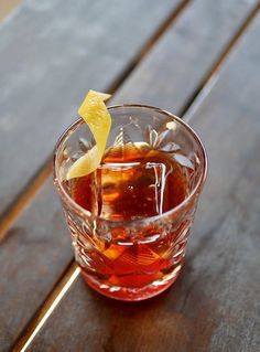 a glass filled with liquid sitting on top of a wooden table next to a slice of lemon